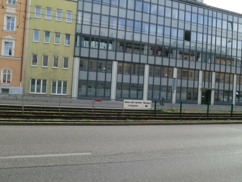 Straße in München mit eigenem Bahnkörper in der Mitte. Mittiger Zaun. Schild "Gleise nicht betreten - Unfallgefahr - Übergang <-"